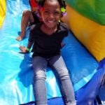 Young girl and young boy slide down an inflatable slide at the Delhi Community Health Center Back to School Block Party.