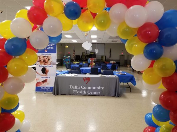 A colorful balloon arch filled iwth yellow blue, red and white balloons makes the entry way vibrant at the Delhi Community Health Center Back to School Block Party.