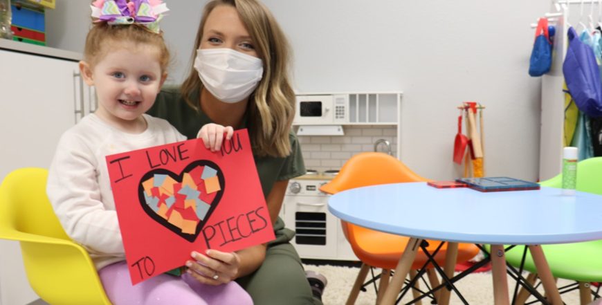 female nurse with child patient holding a craft saying "I Love You To Pieces"