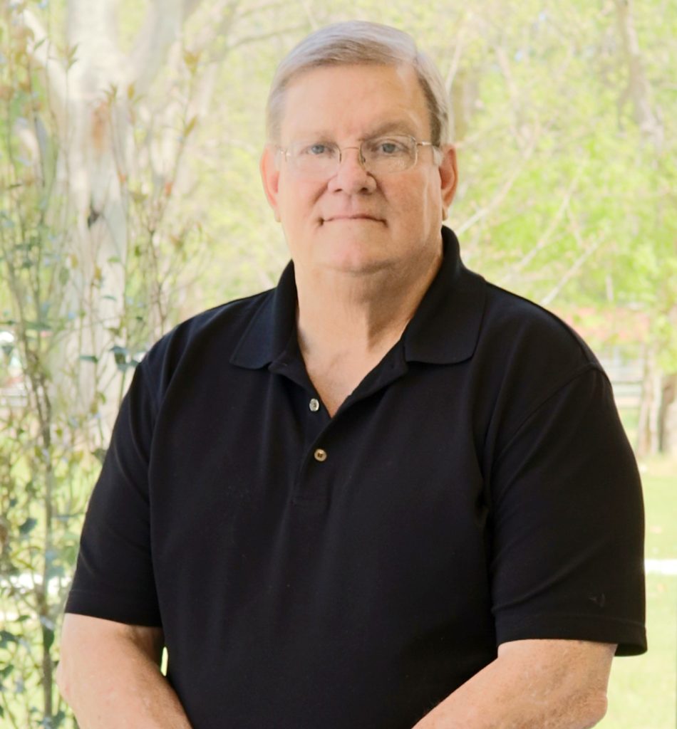 Middle aged man wearing a black shirt smiling at the camera with his arms crossed in front of him